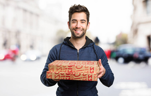 молодий чоловік тримає коробки для піци на розмитому фоні
 - Фото, зображення