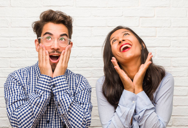 Young indian woman and caucasian man couple surprised and shocked, looking with wide eyes, excited by an offer or by a new job, win concept - Foto, Imagen