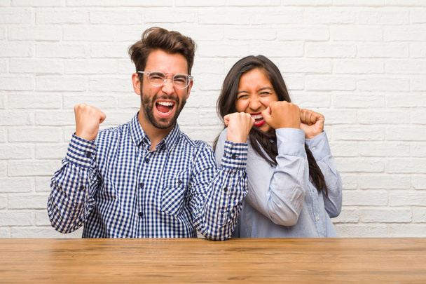 Young indian woman and caucasian man couple very happy and excited, raising arms, celebrating a victory or success, winning the lottery - Photo, Image