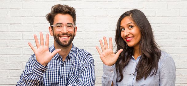 Young indian woman and caucasian man couple showing number five, symbol of counting, concept of mathematics, confident and cheerful - Photo, Image