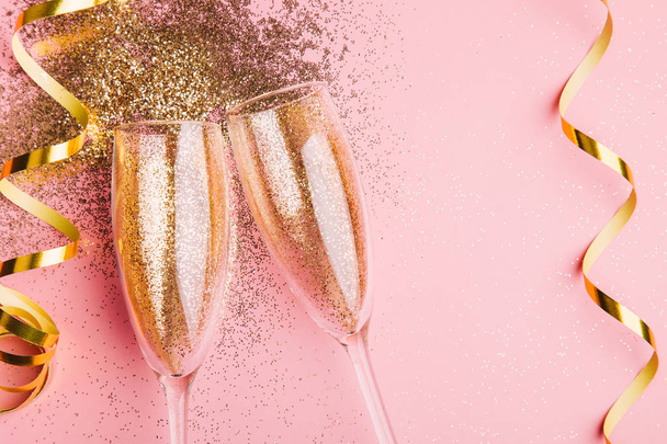 Two glasses of champagne toasting with golden confetti, glitter and serpentine on a pink background. Flat lay. Night of celebration concept - Valokuva, kuva