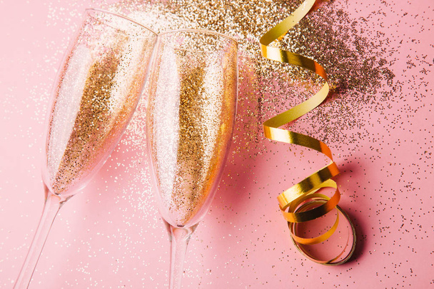 Two glasses of champagne toasting with golden confetti, glitter and serpentine on a pink background. Flat lay. Night of celebration concept - Φωτογραφία, εικόνα