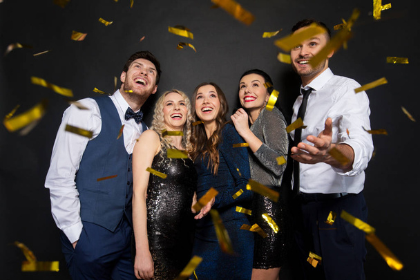happy friends at party under confetti over black - Foto, imagen