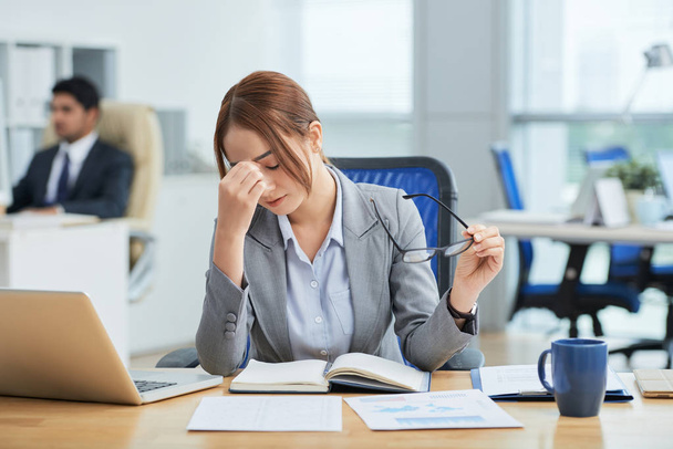 менеджеры сидят за рабочими столами в офисе, уставшая женщина касается носа с закрытыми глазами
  - Фото, изображение