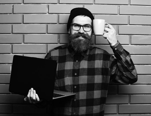 Bearded brutal caucasian hipster holding laptop with cup - Foto, imagen