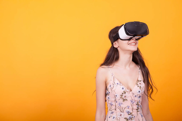 Happy girl getting experience using VR headset glasses of virtual reality in studio over yellow background - Foto, Bild