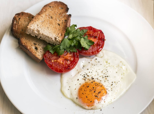 delicioso desayuno con huevo frito, perejil, tostadas y tomates en plato blanco - Foto, Imagen