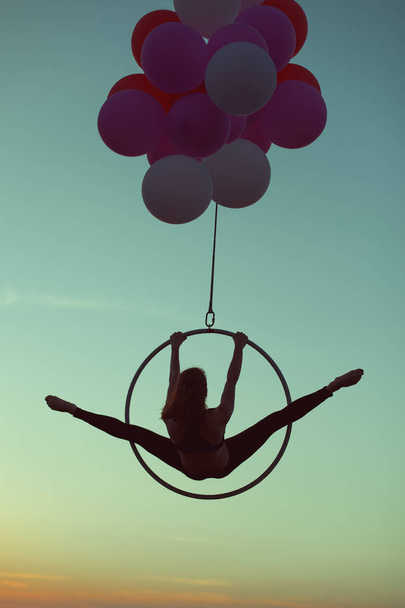 Γυμναστής κορίτσι κάνει ένα σπάγγο σε ένα ακροβατικό δαχτυλίδι στον αέρα στο μπαλόνια. - Φωτογραφία, εικόνα