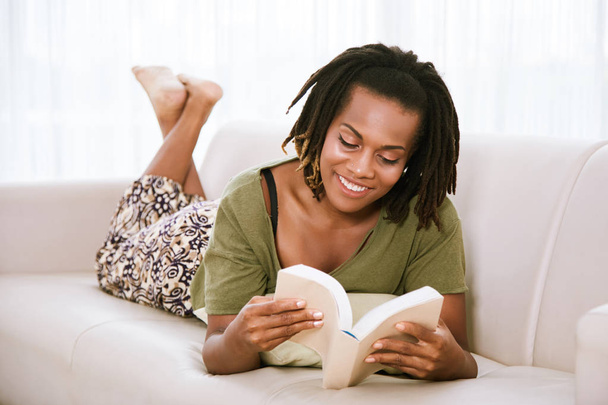 Lachende zwarte vrouw liggend op de Bank en het lezen van een boek - Foto, afbeelding