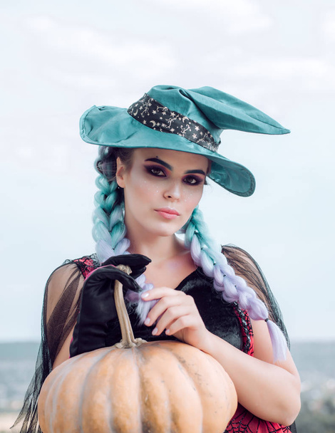 Woman posing with Pumpkin. Halloween Witch with in magic hat. Beautiful young surprised woman in witches hat and costume holding pumpkin. Attractive model girl in Halloween costume. - Zdjęcie, obraz
