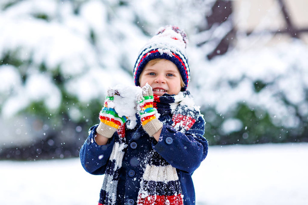 Funny little kid boy in colorful clothes playing outdoors during strong snowfall - Photo, Image