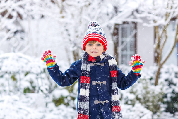 Funny little kid boy in colorful clothes playing outdoors during strong snowfall - Photo, Image