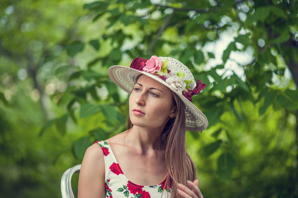 Портрет красивої елегантної жінки в світло-білій сукні і капелюсі, що стоїть в літньому парку
. - Фото, зображення