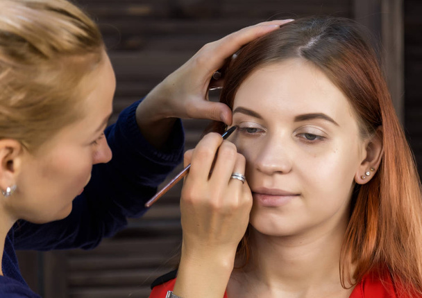 makeup artist preparing young beautiful woman. close-up eyeliner - Fotó, kép