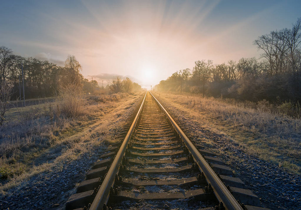 Scenic view of railway going straight ahead through winter field covered by frost to rising sun - Foto, Bild