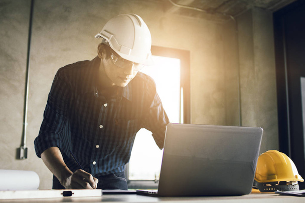Man working, engineering checking, writing on blueprint and looking on laptop at site construction work. - Фото, изображение
