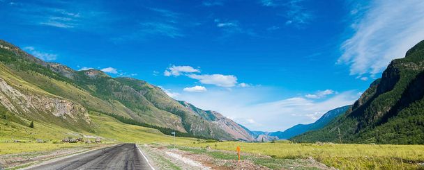 Long panorama of the Altai mountains and roads among them, Altai Republic, Russia. Sunny day in the summer, the blue sky, beautiful mountains on the left and right, the road between them - 写真・画像