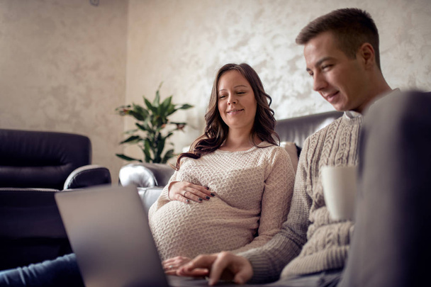 Fiatal család-terhes nő és a férje dívány otthon ül. - Fotó, kép