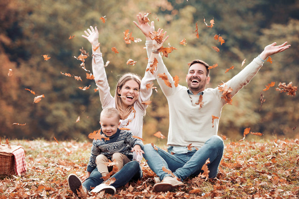 szczęśliwe rodziny posiadające zabawy rzucanie jesień liści w parku w świetle dziennym - Zdjęcie, obraz