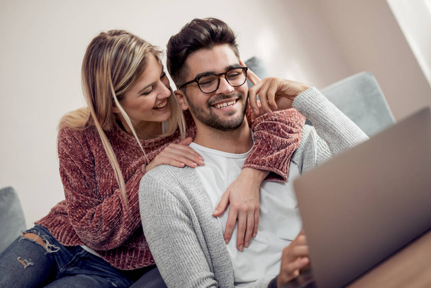 Couple heureux se détendre sur leur canapé et en utilisant un ordinateur portable, souriant à la maison
. - Photo, image