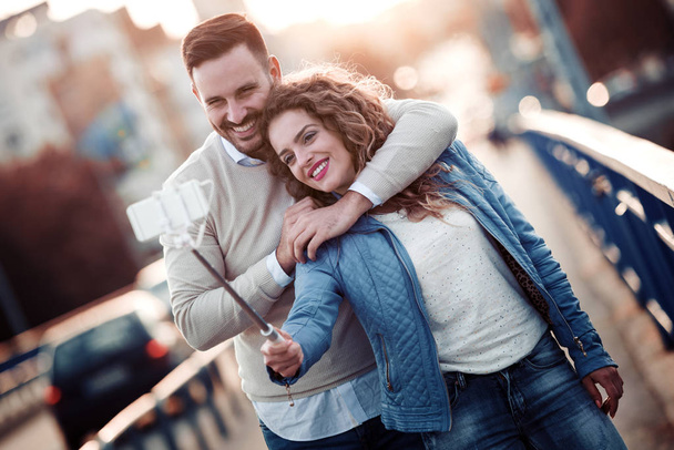 Mutlu genç çift alarak selfie Caddesi üzerinde bir selfie sopa ile cep telefonu ile. - Fotoğraf, Görsel