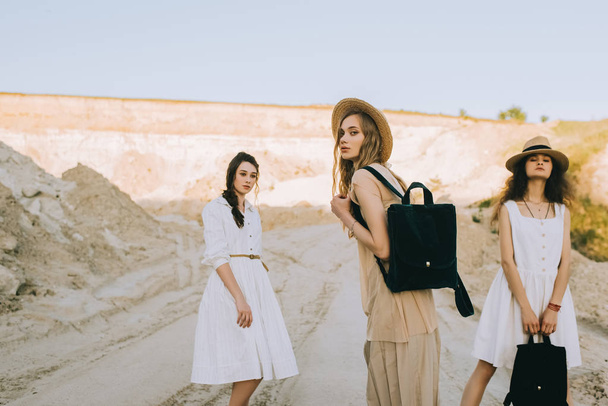 elegant stylish girlfriends in straw hats walking with backpacks in sandy canyon - 写真・画像