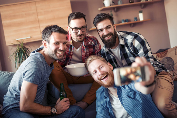 Cheerful group of friends having fun at home,taking selfie and watching football game. - Foto, afbeelding