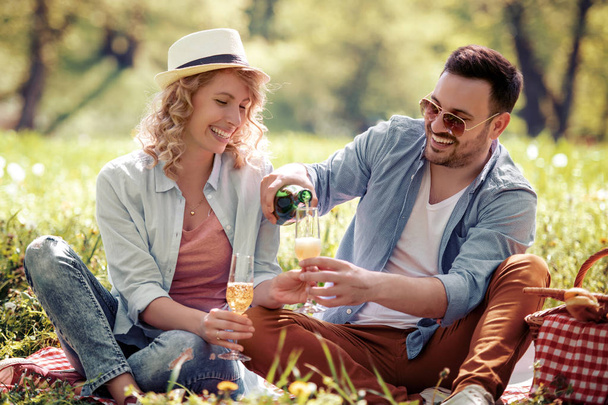 Happy attractive couple sitting together and drink wine on picnic.  - Photo, Image