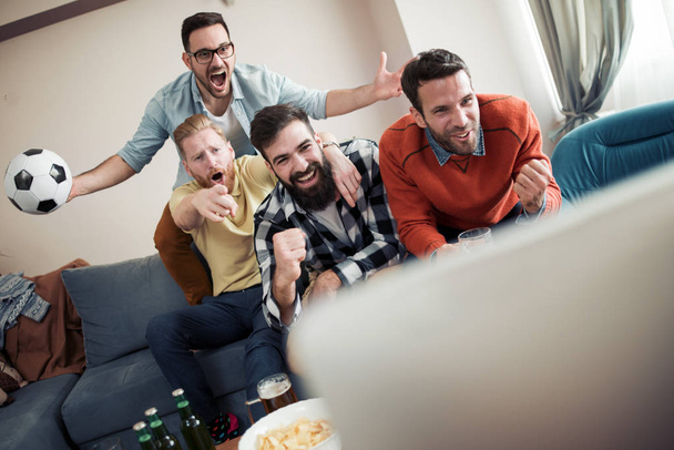 Grupa przyjaciół, oglądając mecz piłki nożnej w telewizji i świętuje bramkę. - Zdjęcie, obraz