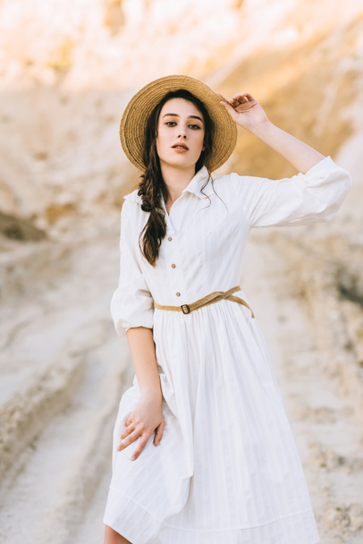 charming stylish girl posing in white dress and straw hat in sandy canyon - 写真・画像