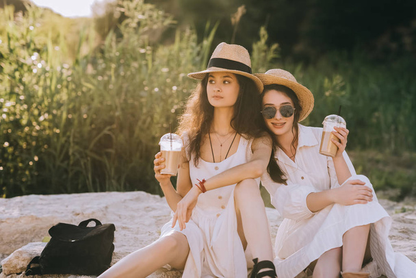 kauniit tytöt tyylikkäissä mekoissa kuppeja kahvia latte istuu maassa
 - Valokuva, kuva