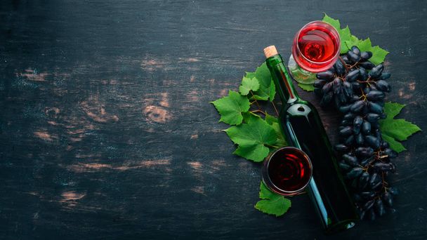 Red wine in a bottle with a glass and grapes. On a black wooden background. Free space for text. Top view. - Zdjęcie, obraz