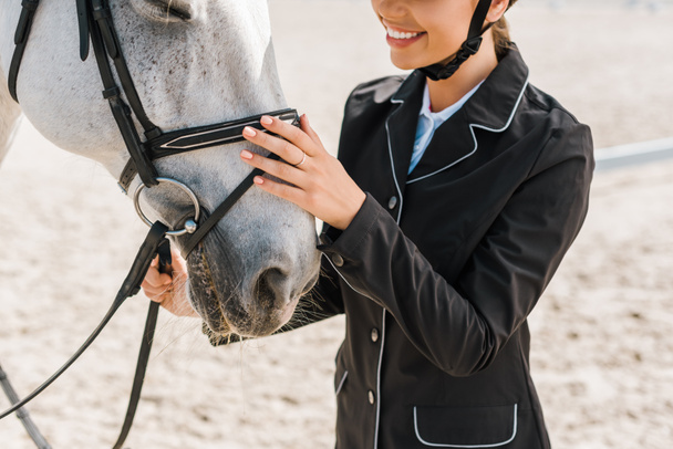 cropped image of smiling female equestrian palming horse at horse club - Photo, Image
