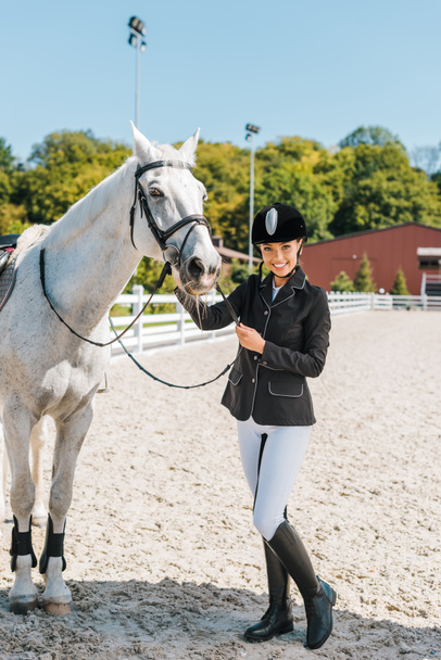 Lächelnde attraktive Reiterin blickt in die Kamera neben Pferd im Pferdeclub - Foto, Bild