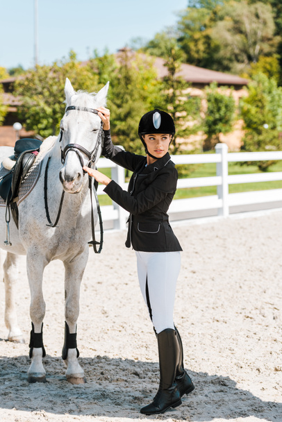 привлекательная женщина конница фиксирует лошадиный холтер и смотрит в сторону конного клуба
 - Фото, изображение