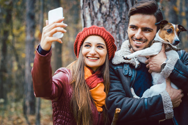 女性と電話 selfie を取って秋散歩に自分の犬を持つ男 - 写真・画像