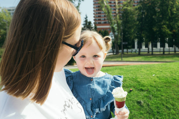 Young mother carrying a 3 years old child eating ice cream in a city park on a warm sunny day - Foto, immagini