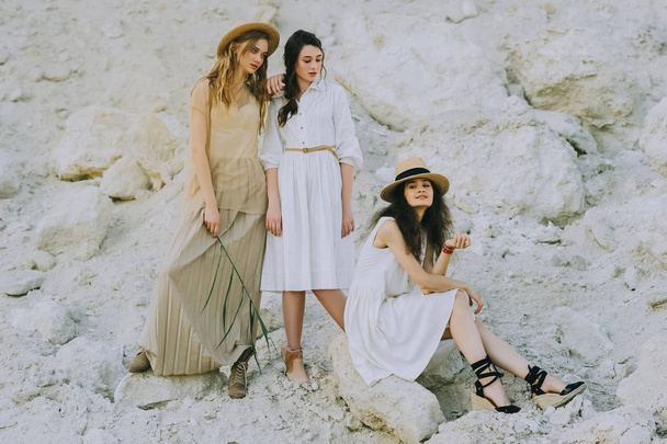 hermosos amigos en vestidos elegantes y sombreros de paja posando juntos en cañón de arena
 - Foto, imagen