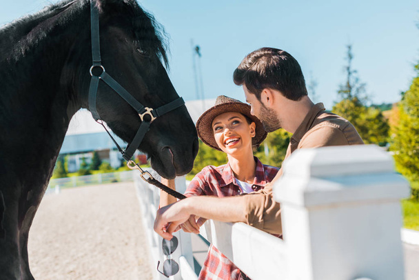 cow-boy souriant et cow-girl debout près du cheval au ranch et se regardant
 - Photo, image
