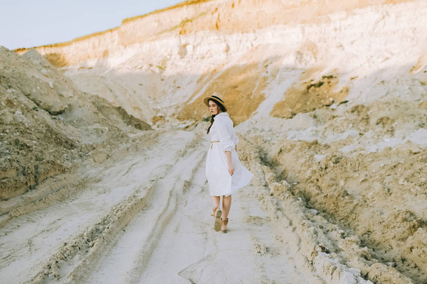 стильна дівчина в білій сукні і солом'яному капелюсі, що йде в піщаному каньйоні
 - Фото, зображення
