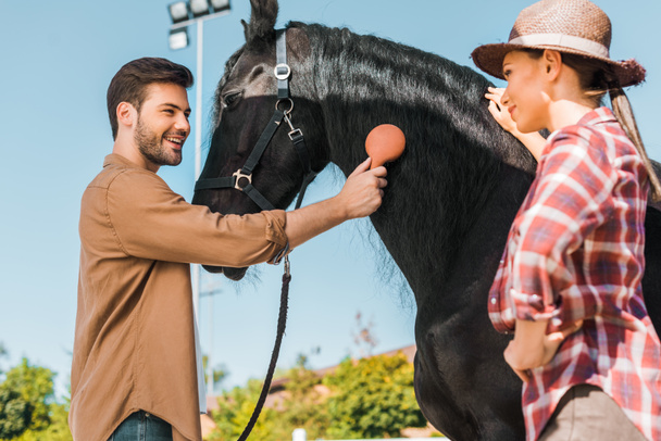 όμορφος χαμογελώντας ιππασίας κτενίσματος μαύρο άλογο χαίτη στο ranch - Φωτογραφία, εικόνα