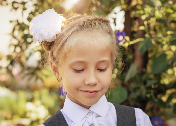 Γέλιο κορίτσι στο σχολείο στολή με ένα τόξο στο κεφάλι της το φθινόπωρο του πάρκου. Πορτρέτο του ένα όμορφο κορίτσι σχολικής ηλικίας. - Φωτογραφία, εικόνα