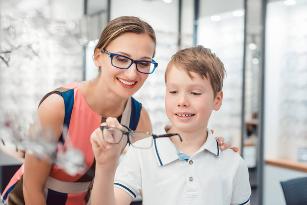 Mother and son both liking the eyeglasses offered in optician shop being excited  - Photo, Image