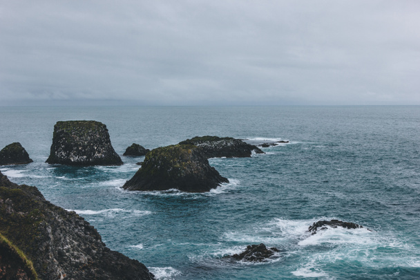 dramatický snímek hornin v modrém oceánu v Arnarstapi, Island na zamračený den - Fotografie, Obrázek
