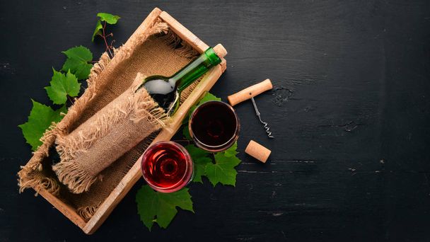 Red wine in a bottle with a glass and grapes. On a black wooden background. Free space for text. Top view. - Fotoğraf, Görsel