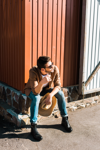 cowboy bonito em óculos de sol sentado e fumar cigarro no rancho
 - Foto, Imagem