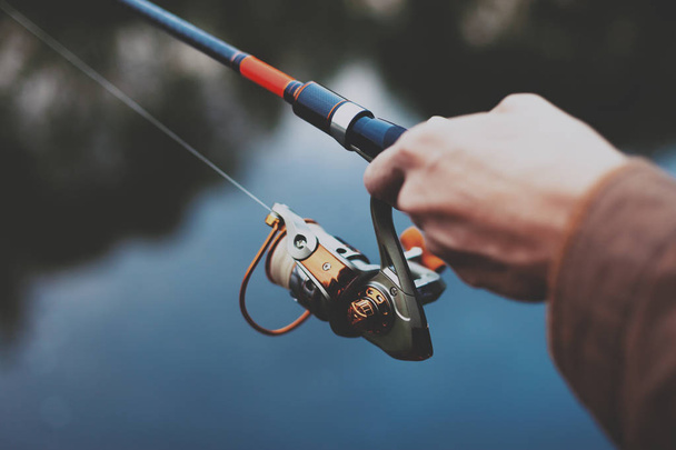 Young fisherman is fishing in river with spinning. Hobby and outdoor activities concept - Foto, Imagem