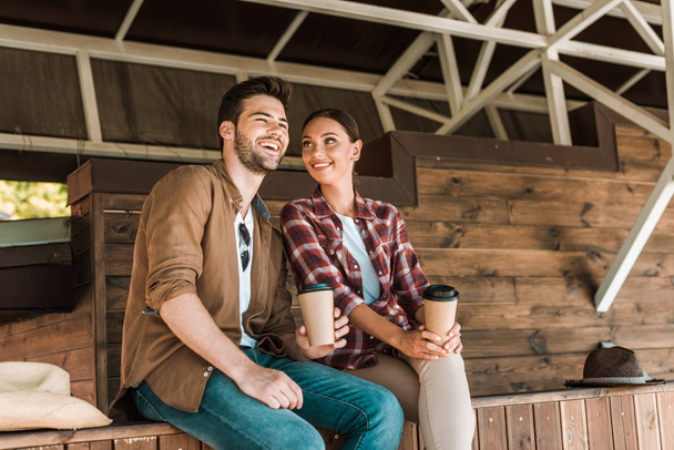 smiling man and woman sitting with disposable coffee cups at ranch - Foto, Imagem