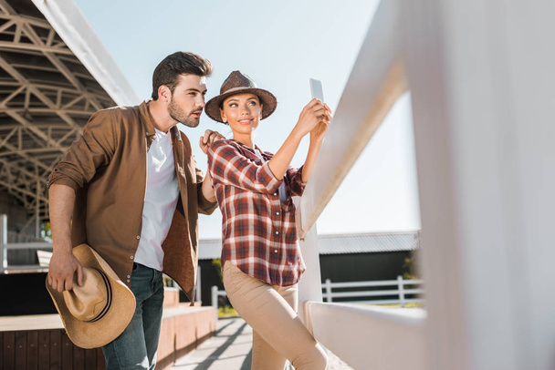 selectieve aandacht voor stijlvolle ruiters in casual kleding nemen selfie met smartphone op ranch - Foto, afbeelding