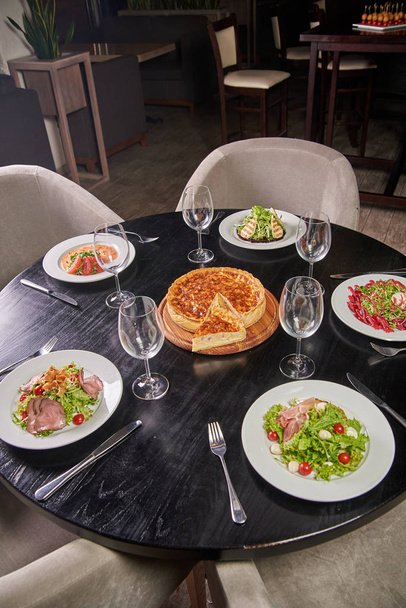 Elegante mesa negra con una variedad de deliciosos platos del chef en una cafetería, restaurante. La mesa de comedor está lista y reservada para los huéspedes. Pastel de queso en el centro de la mesa
. - Foto, imagen